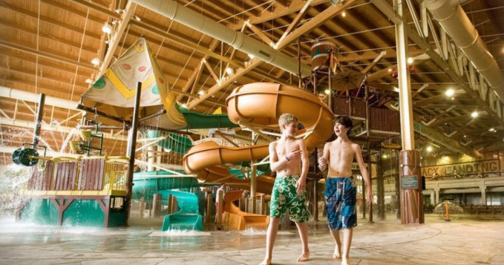 two boys in swim trunks walking in front of indoor water slides