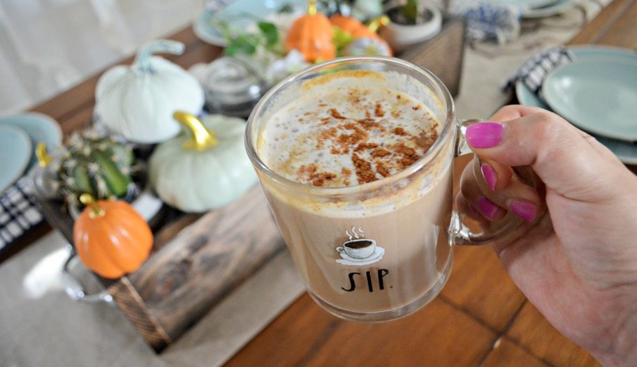 hand holding pumpkin spice latte in front of tablescape