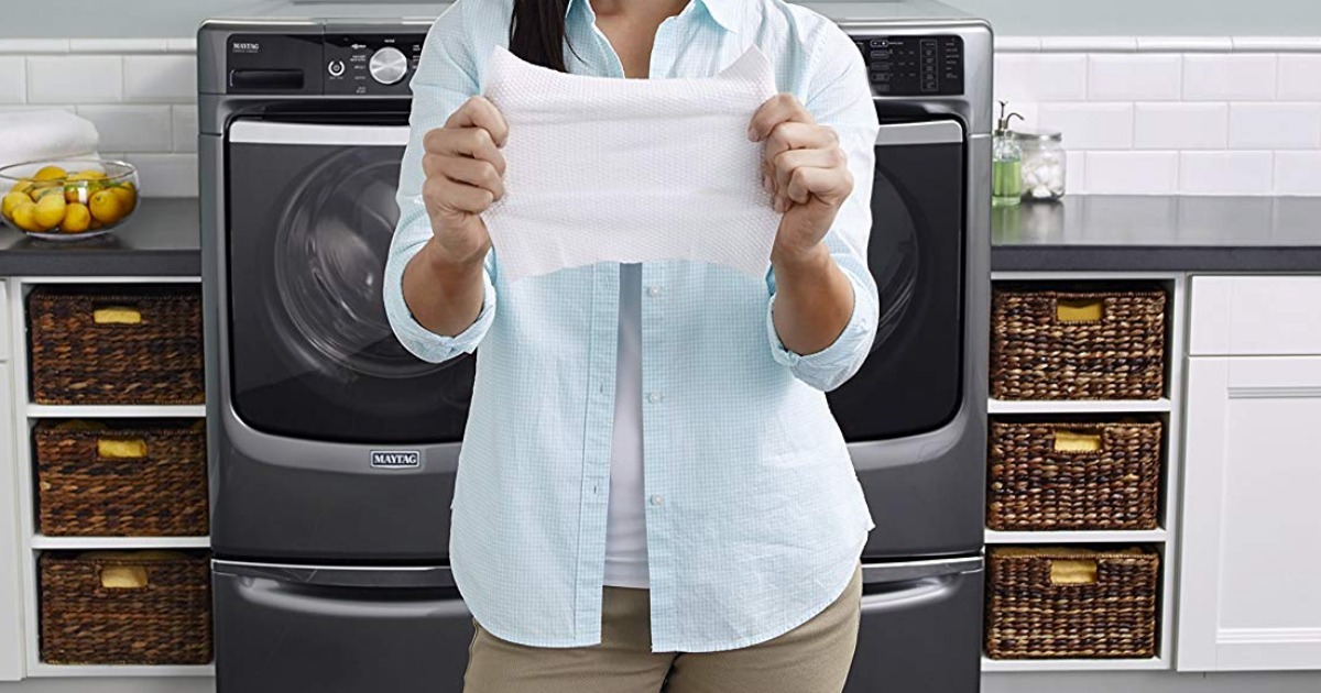 woman standing in front of a washing machine and dryer holding up a cleaning cloth