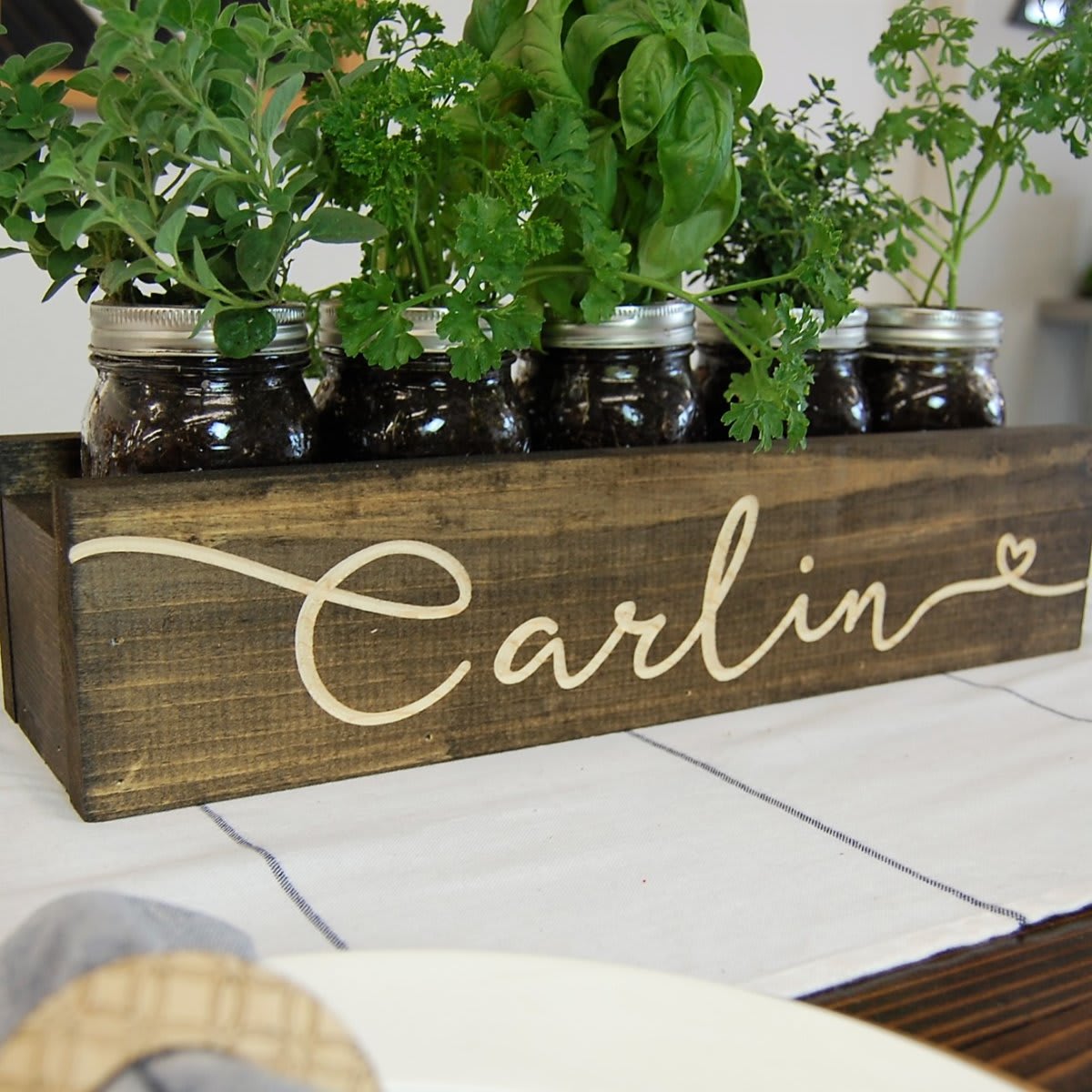 wooden planter box that reads Carlin with mason jars and herbs