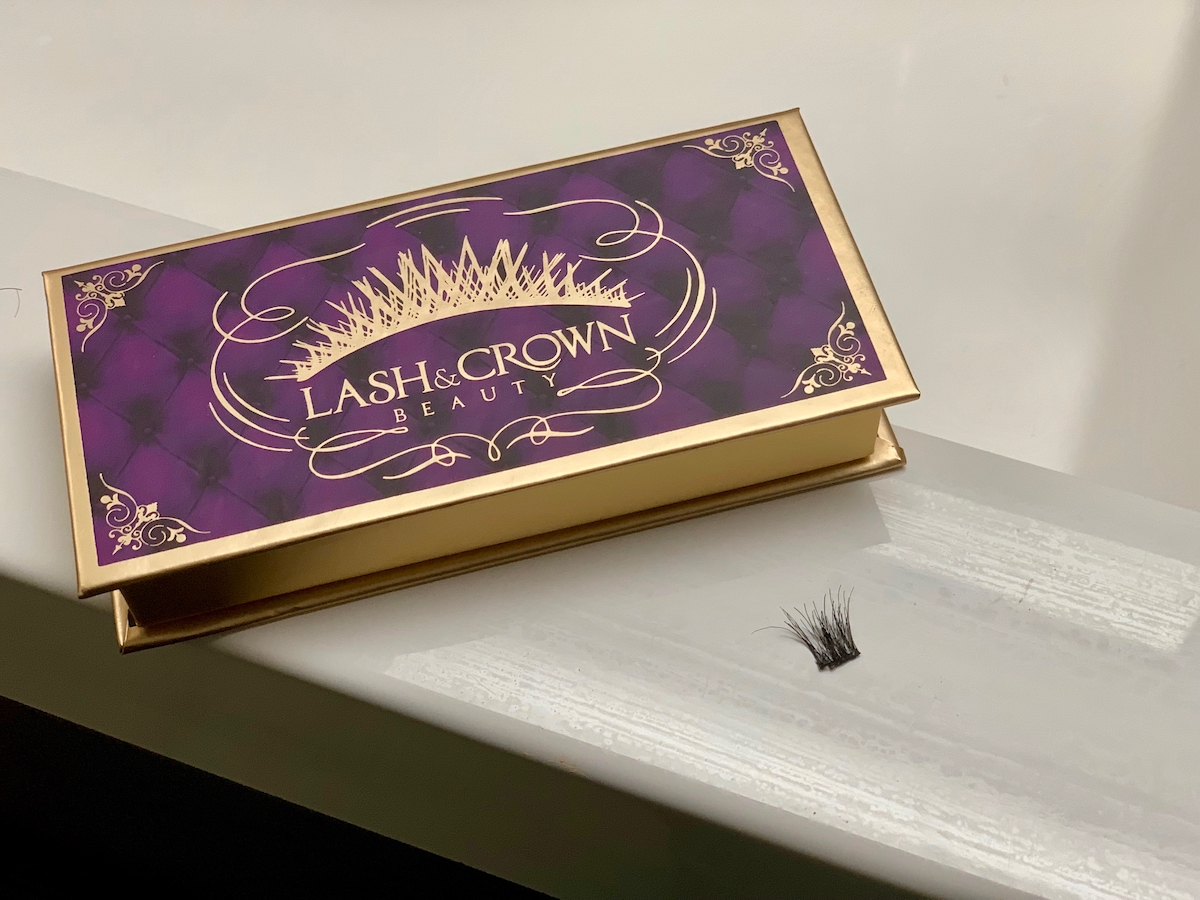 purple and gold lash and crown box with piece of false eyelashes on white ledge