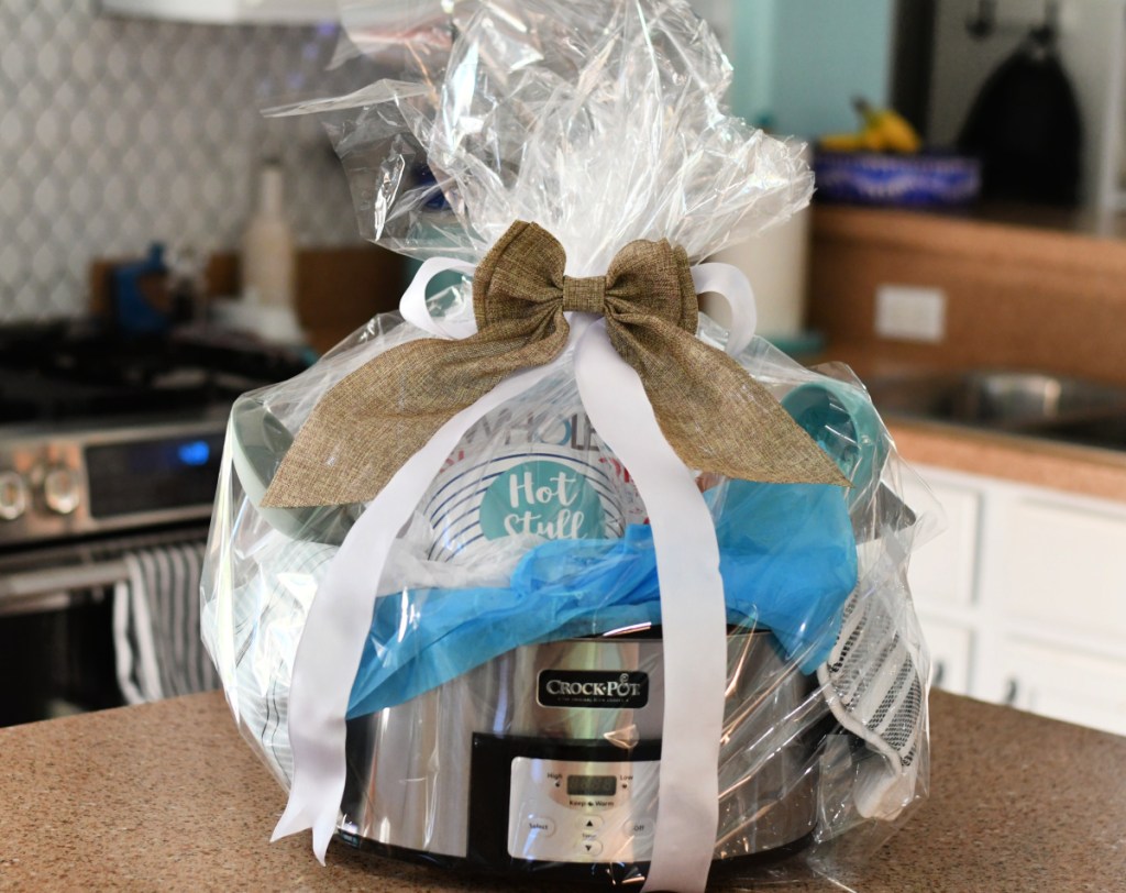 A Crock pot slow cooker wrapped up in cellophane with food-related gift basket items