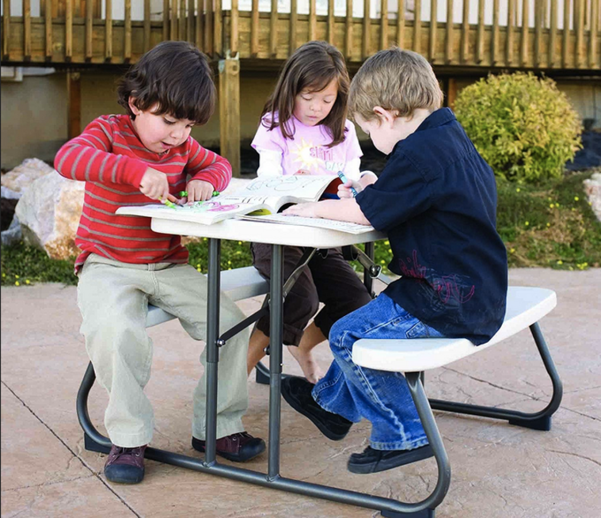 two boys and a girl sitting at a kids picnic table
