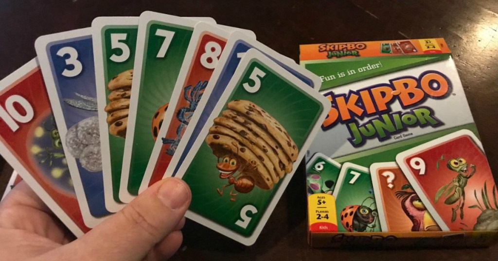 hand holding skipbo cards in front of box laying on black table