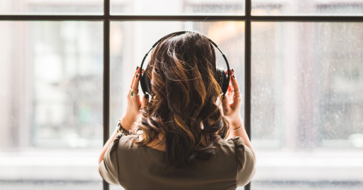 woman listening to headphones standing in front of window