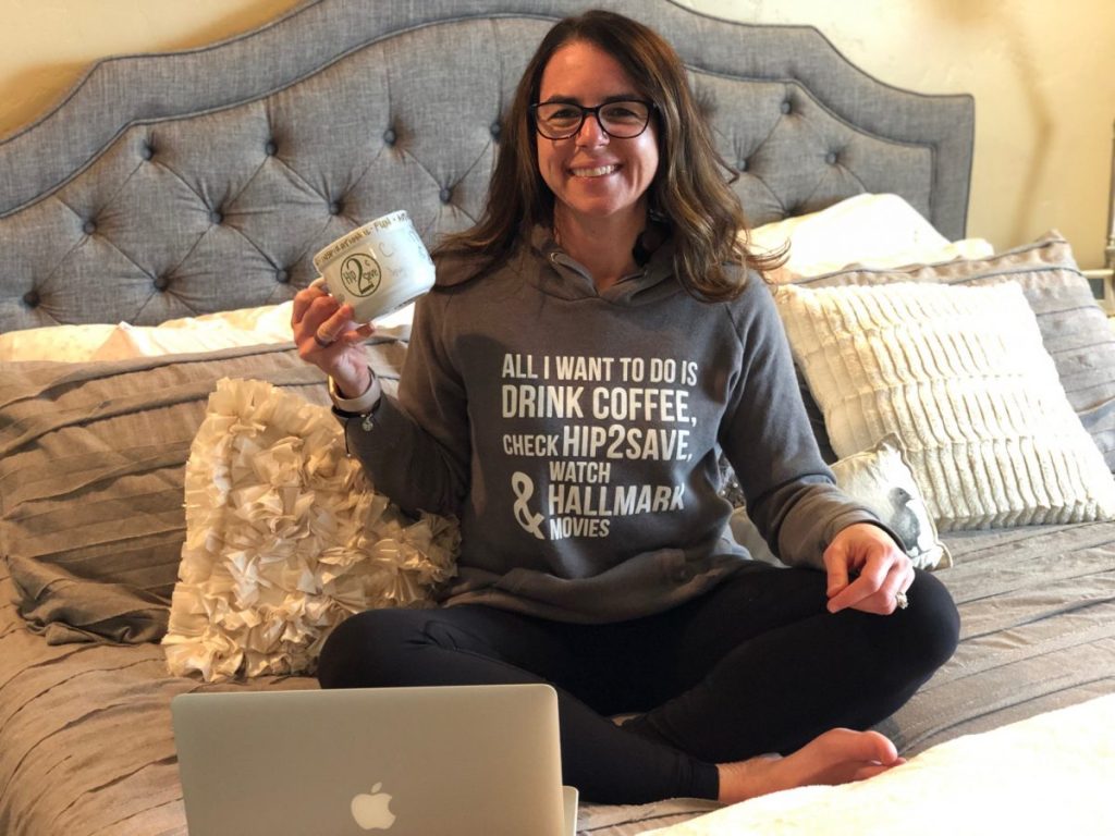 woman sitting on bed with sweatshirt holding coffee cup 