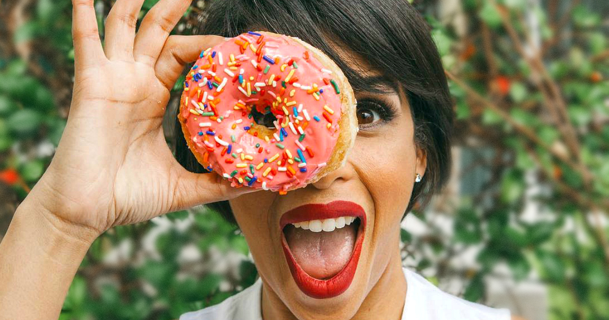 woman holding a donut over her eye and smiling