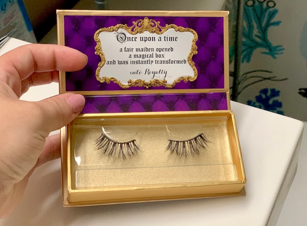 hand holding a gold and purple box with faux lashes