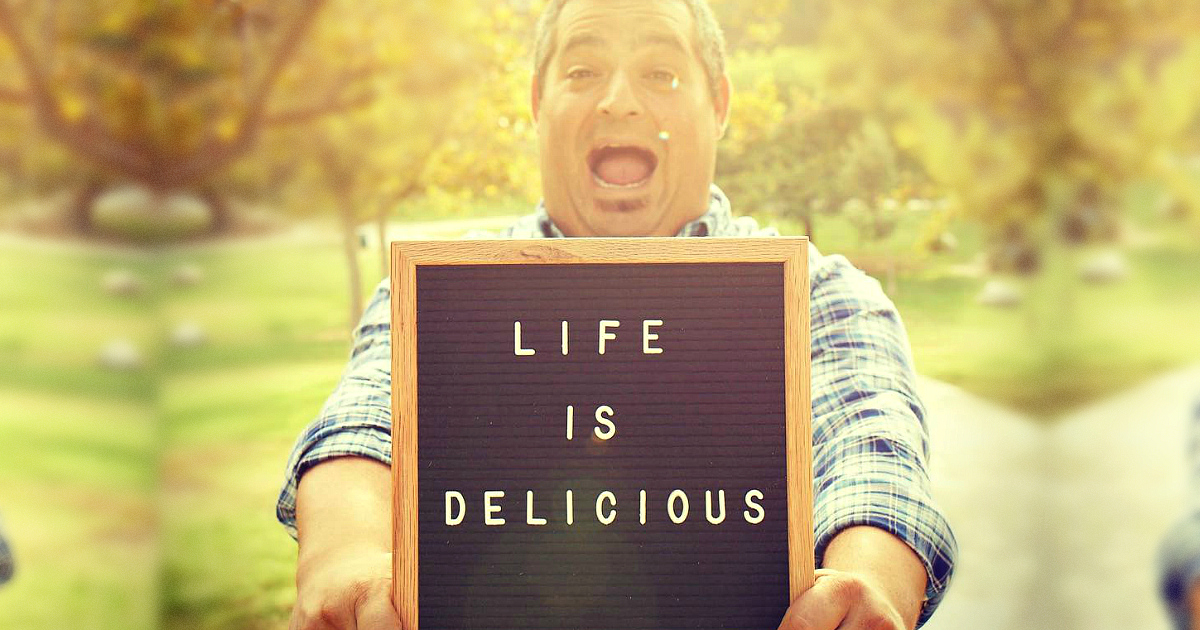 man holding a "life is delicious" sign
