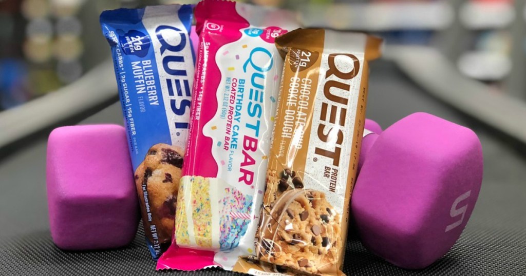 Three Quest Bars in different flavors propped up next to Dumbells