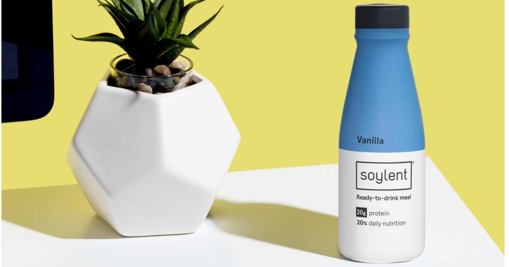 Soylent Vanilla Bottle on table with a plant in a white vase next to it