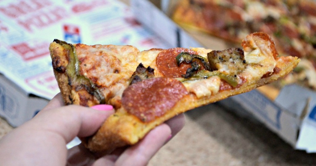 hand holding dominos pizza with pepperoni and jalapenos