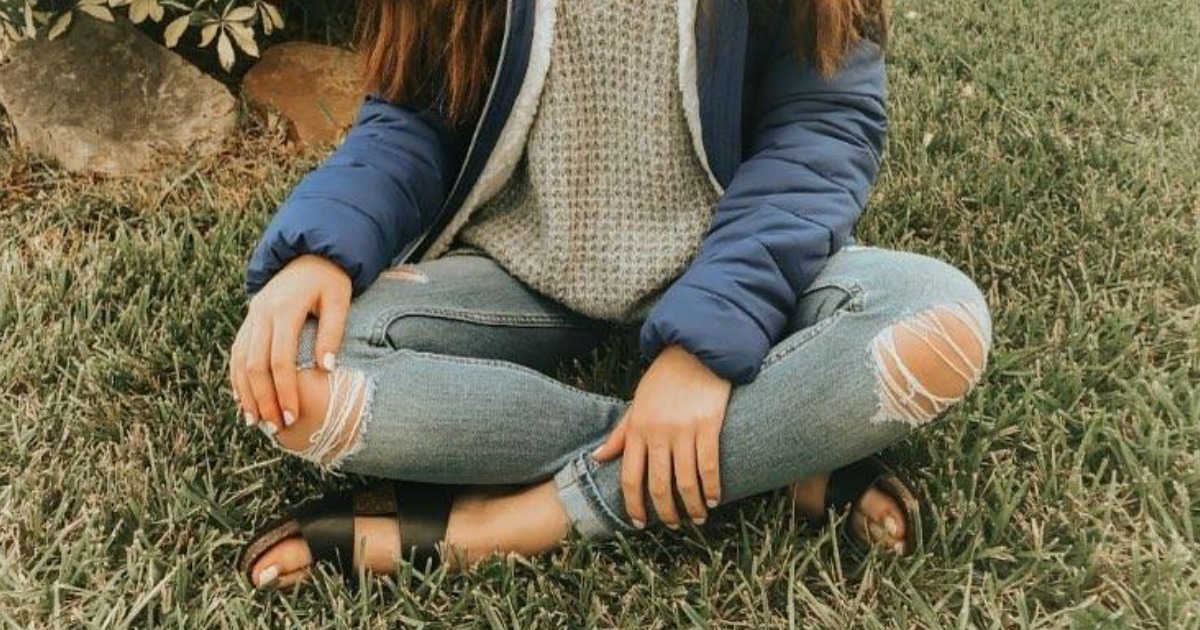 woman sitting cross-legged on the ground wearing torn jeans