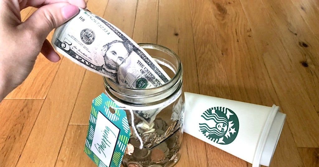 putting $5 bill in shopping money jar with Starbucks cup on the side 