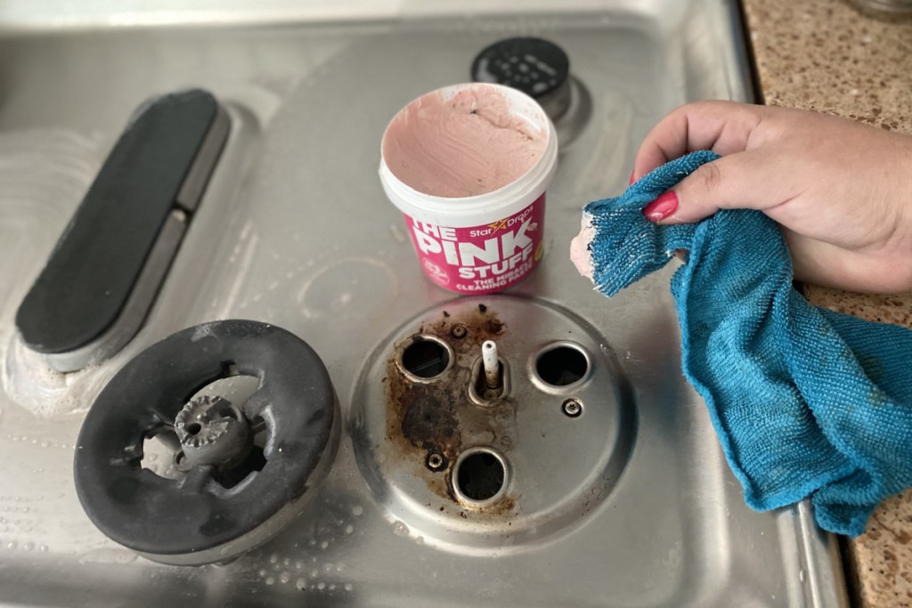 Hand holding a rag with The Pink Stuff cleaner on stovetop