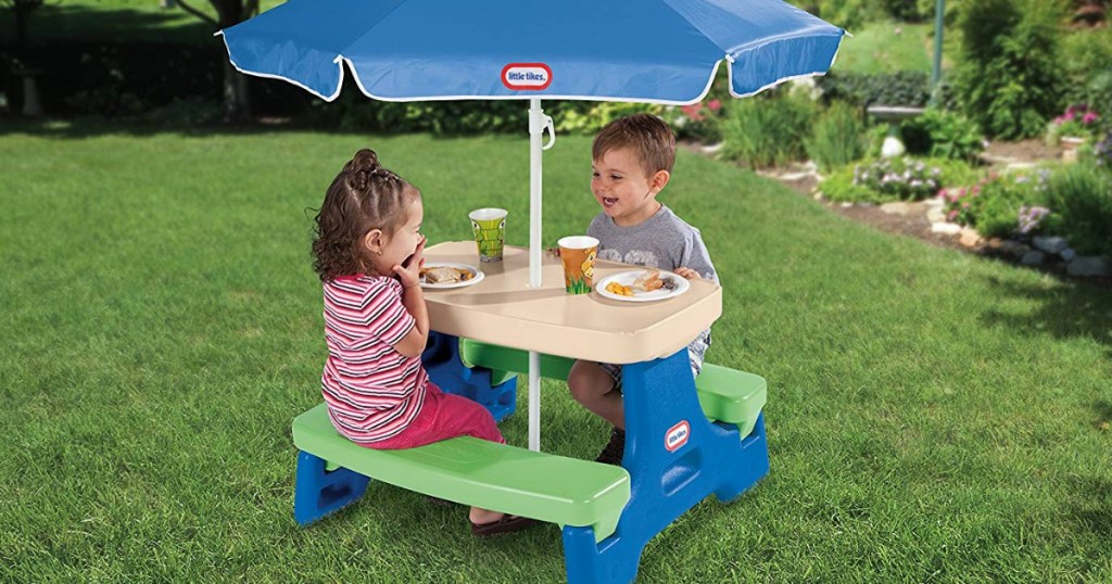 two kids sitting at a plastic table with umbrella