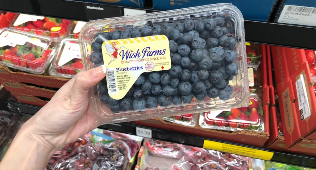 hand holding fresh blueberries with cartons of strawberries in the background