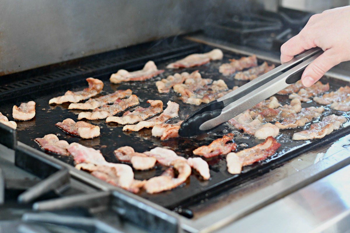 large stovetop griddle of cooked bacon 