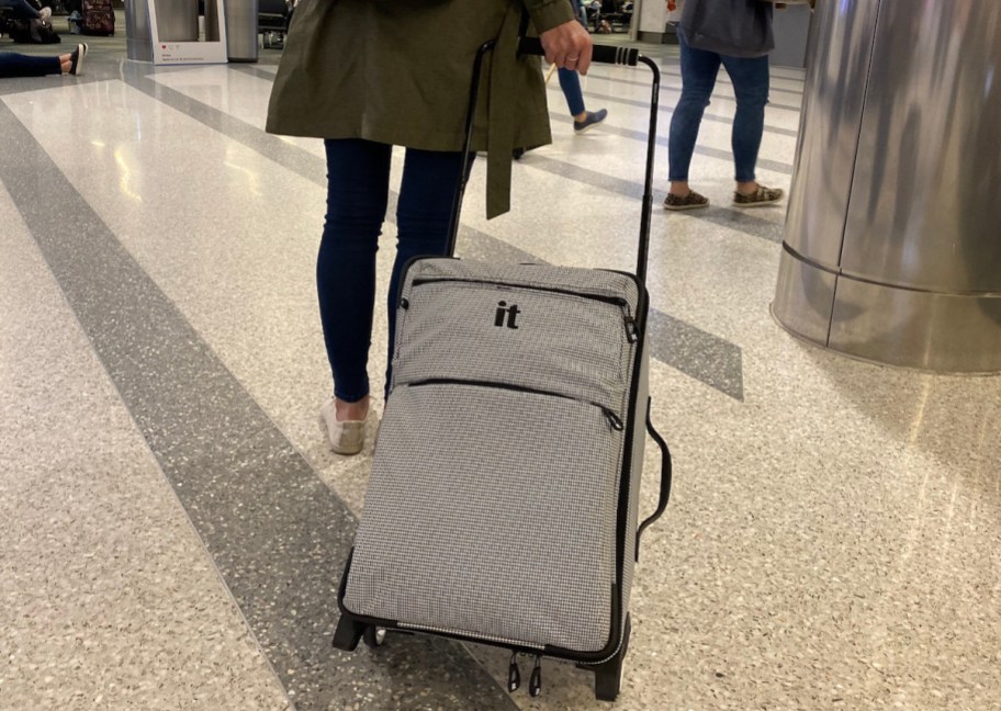 woman walking in airport pulling gray it carry on luggage