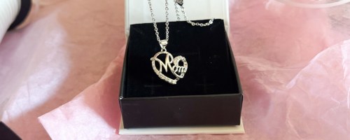 person holding cate & chloe persephone mom necklace in front of box with pink tissue paper