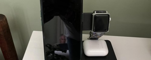 wireless charger in black sitting on table charging phone, apple watch, and airpods