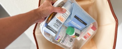 clear travel kit filled with sunscreen, makeup wipes, medicine and mouthwash being put into tote bag