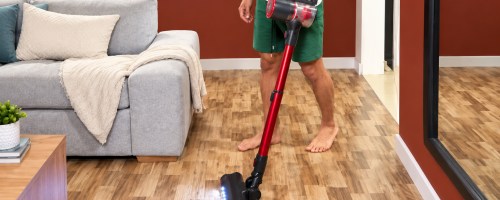Man using lighted cordless vacuum in living room with wooden floor