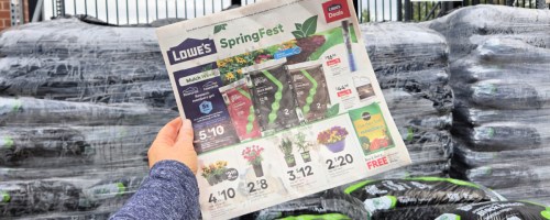 Woman holding a Lowe's SpringFest ad in front of mulch