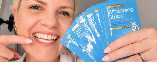 Woman holding up packets of white strips and pointing to her teeth