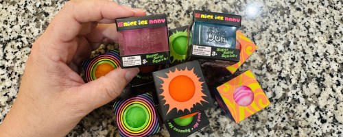 hand reaching for a NeeDoh Teenie toy above an assortment of them