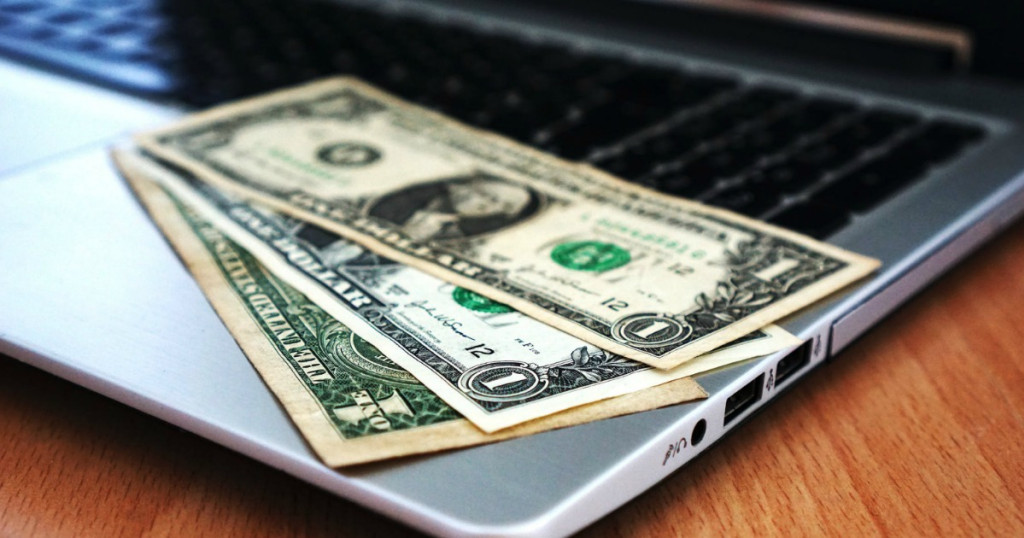 three one dollar bills laying on the corner of a laptop