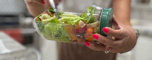 Woman, eating salad with a fork out of a glass salad pod