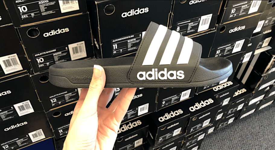 black and white adidas slides in-hand in front of black shoe boxes