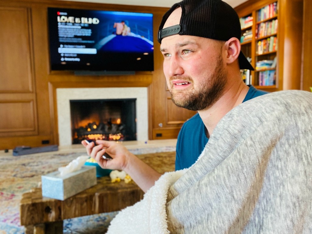 man with sad face wearing blanket and watching tv