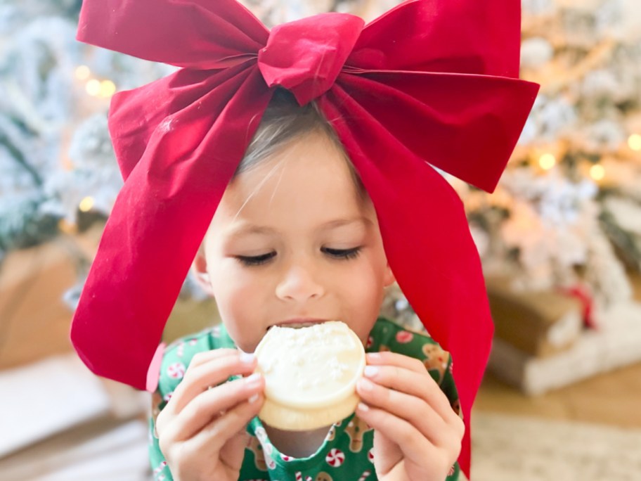 girl with big red bow on her head eating a cookie