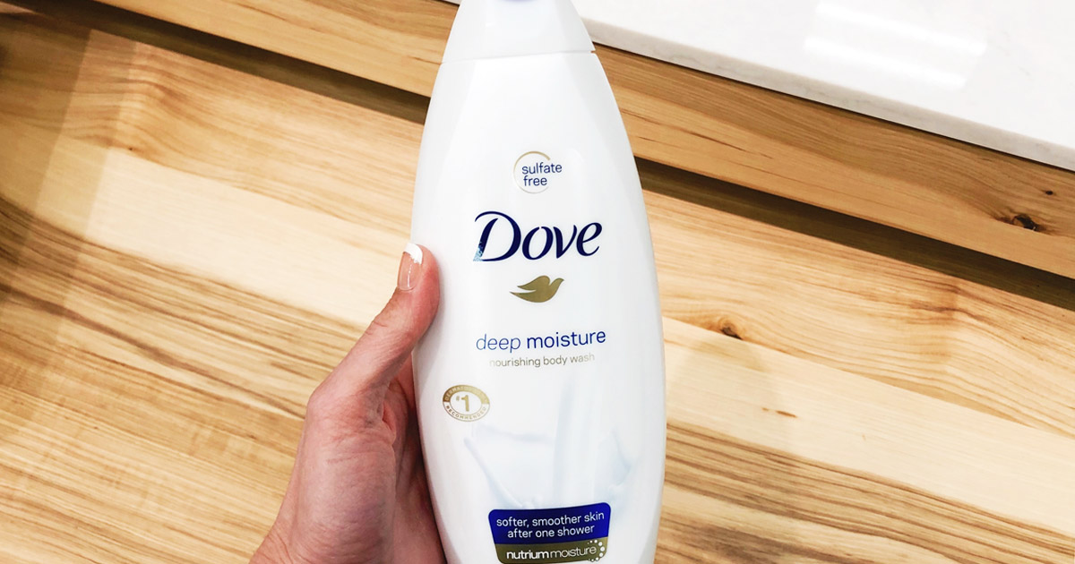 hand holding a bottle of dove body wash above a blond wood floor