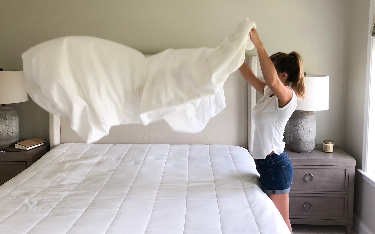 woman throwing blanket high in the air over bed