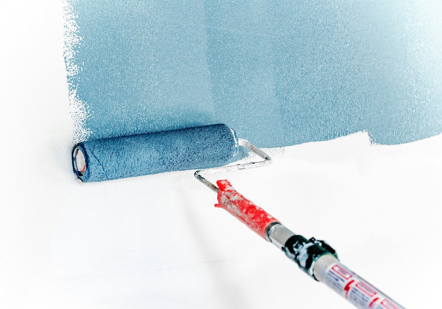 paint roller with blue paint rolling on white wall