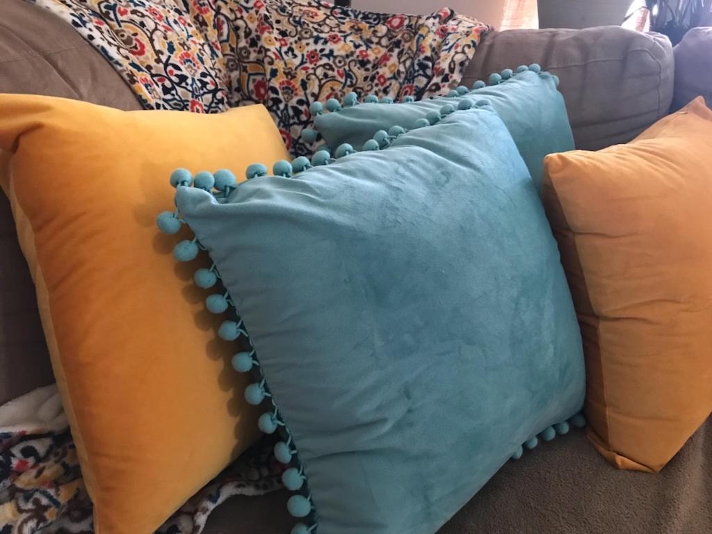 4 pom pom pillows on couch with yellow and blue
