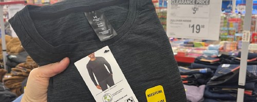 woman holding up a black folded shirt in front of a clearance sign