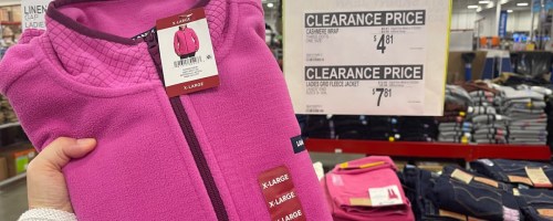 woman holding a pink jacket in front of a clearance sign