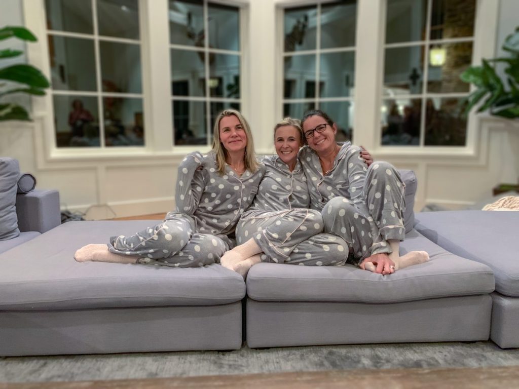 Women in matching pajamas sitting on gray couch in living room by big windows