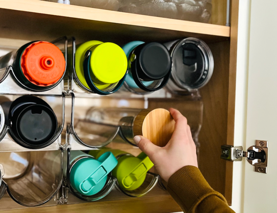 woman grabbing a reusable water bottle from a stackable storage unit in a cabinet
