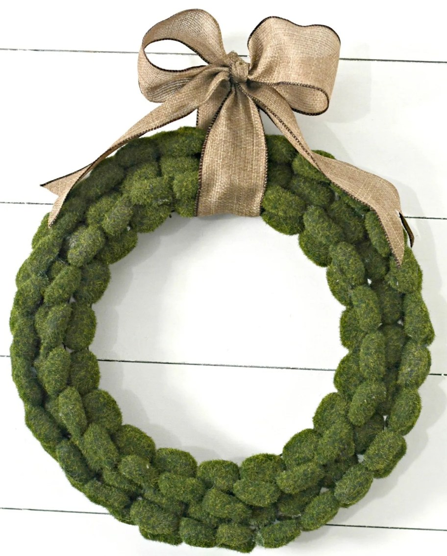moss wreath with burlap bow hanging on shiplap wall