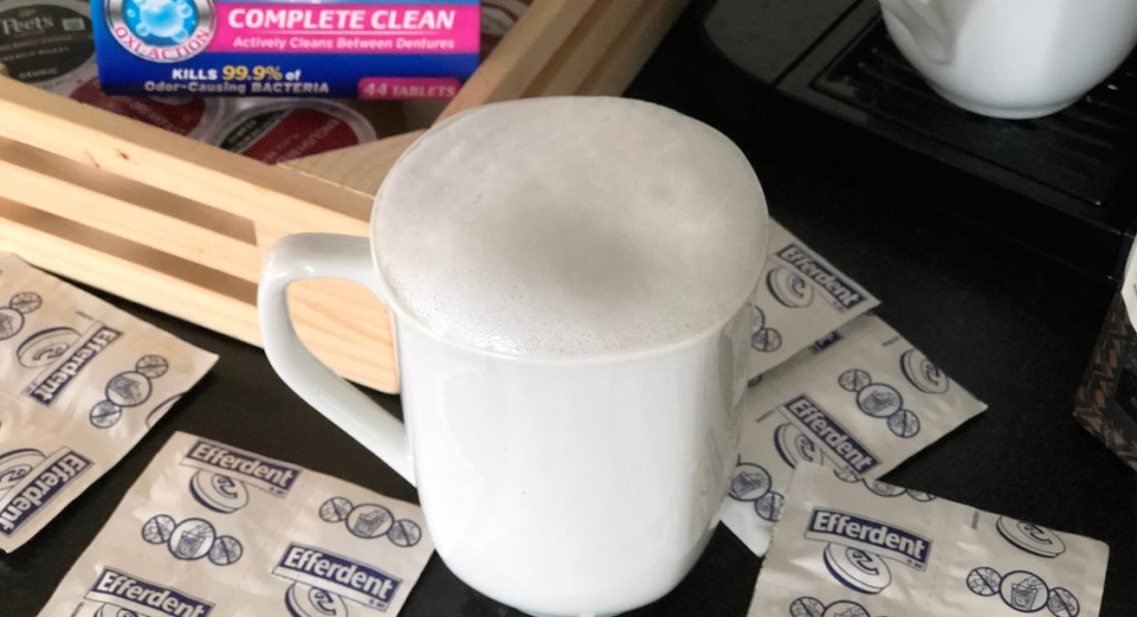 foaming white coffee mug with denture tablet packs sitting on black countertop