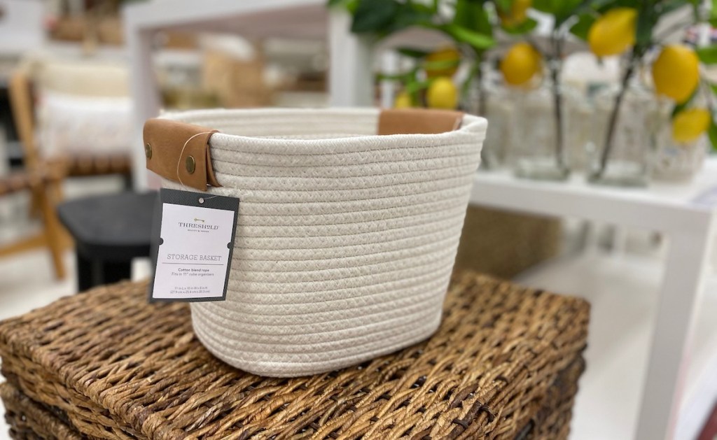 white basket with brown leather handles with white tag sitting in store on wicker furniture