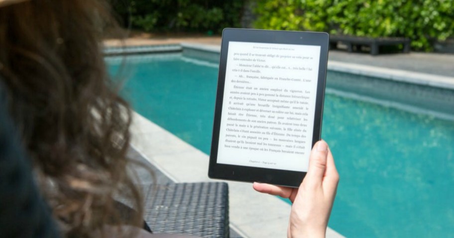 woman reading ebook on kindle near a pool