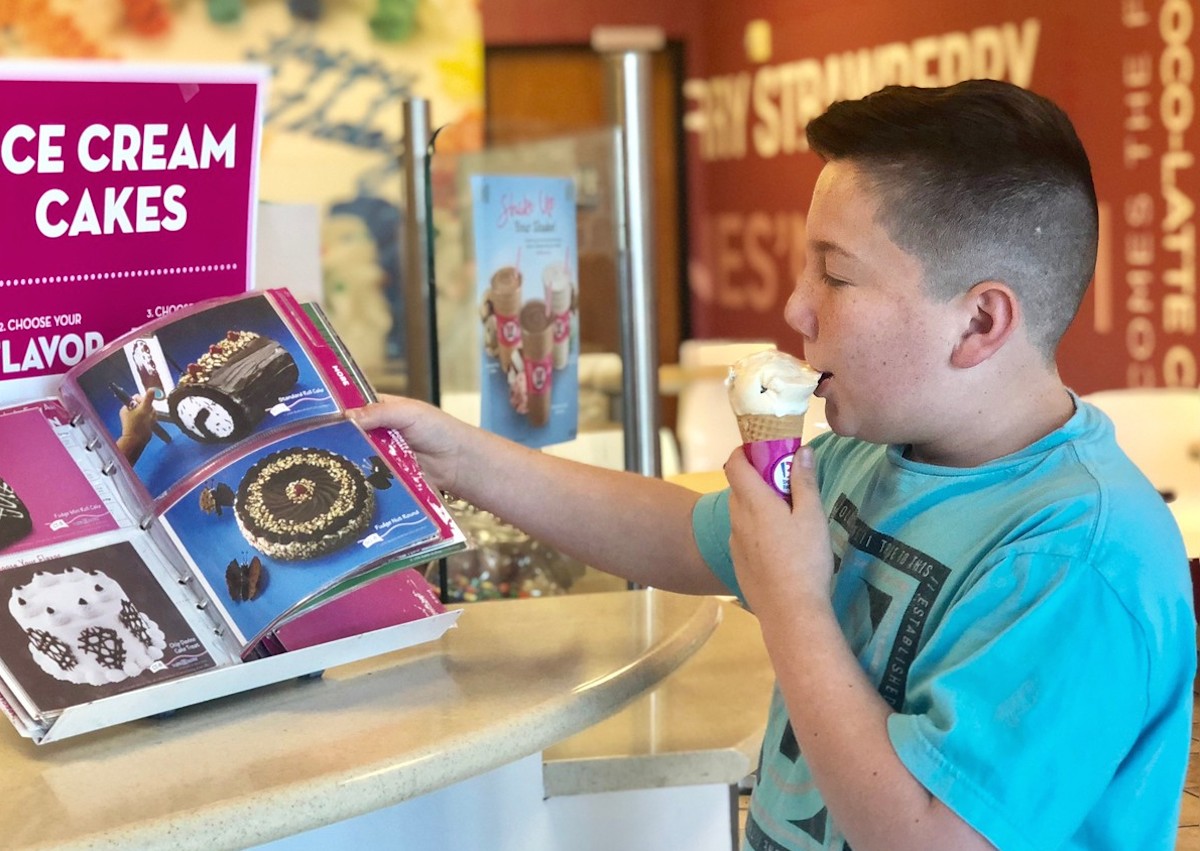boy eating a scoop of vanilla cone ice cream looking at book with cakes