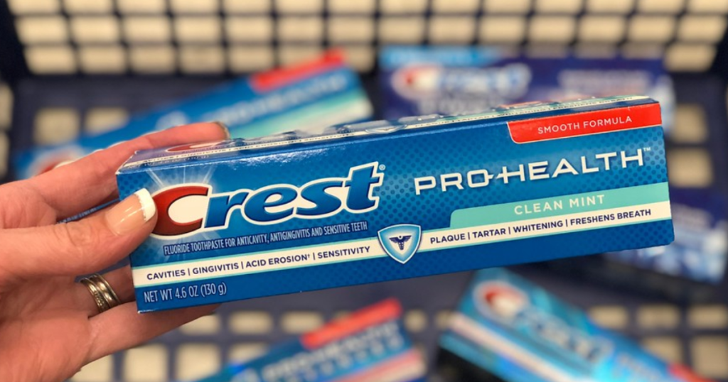 hand holding box of Crest pro-health toothpaste over shopping basket