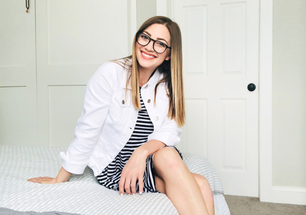 woman wearing white denim jacket sitting on bed smiling